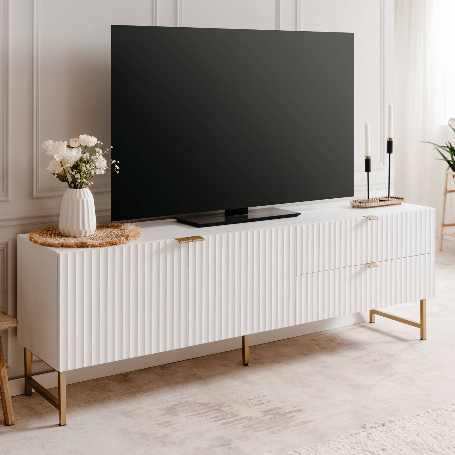 TV-Lowboard in Weiß mit Schubladenstauraum. Der Artikel ist freigestellt auf weißem Hintergrund abgebildet. Sichtbare Details sind geschlossene Schranktüren, Schubladenfronten und goldfarbene schlanke Beine.