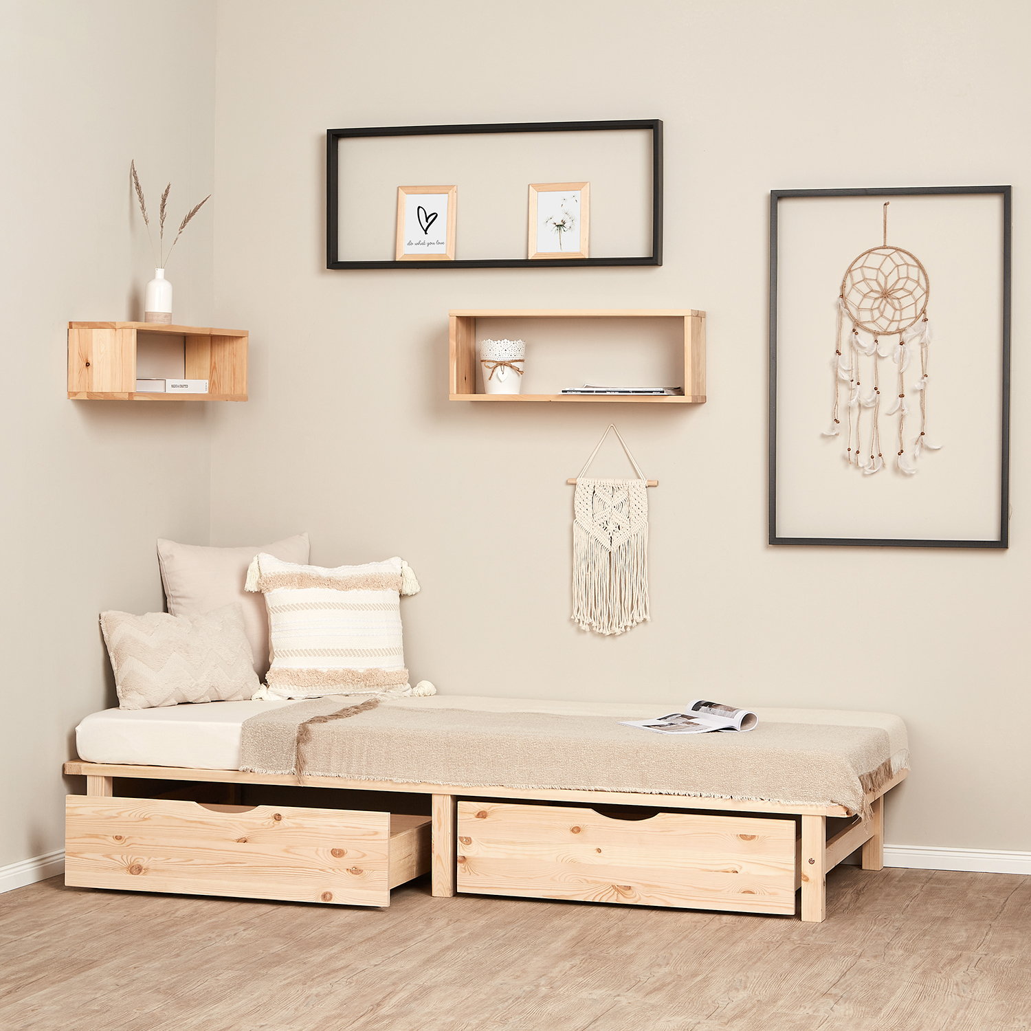 Bettgestell in Palettenform in Naturholzfarbe mit Holzelementen, Lattenrost und Stauraum. Das niedrige Bett ist mit einer Matratze und einer länglichen Polsterrolle vor weißem Hintergrund abgebildet. Die umlaufenden Rahmenleisten und die kurzen Beine sind
