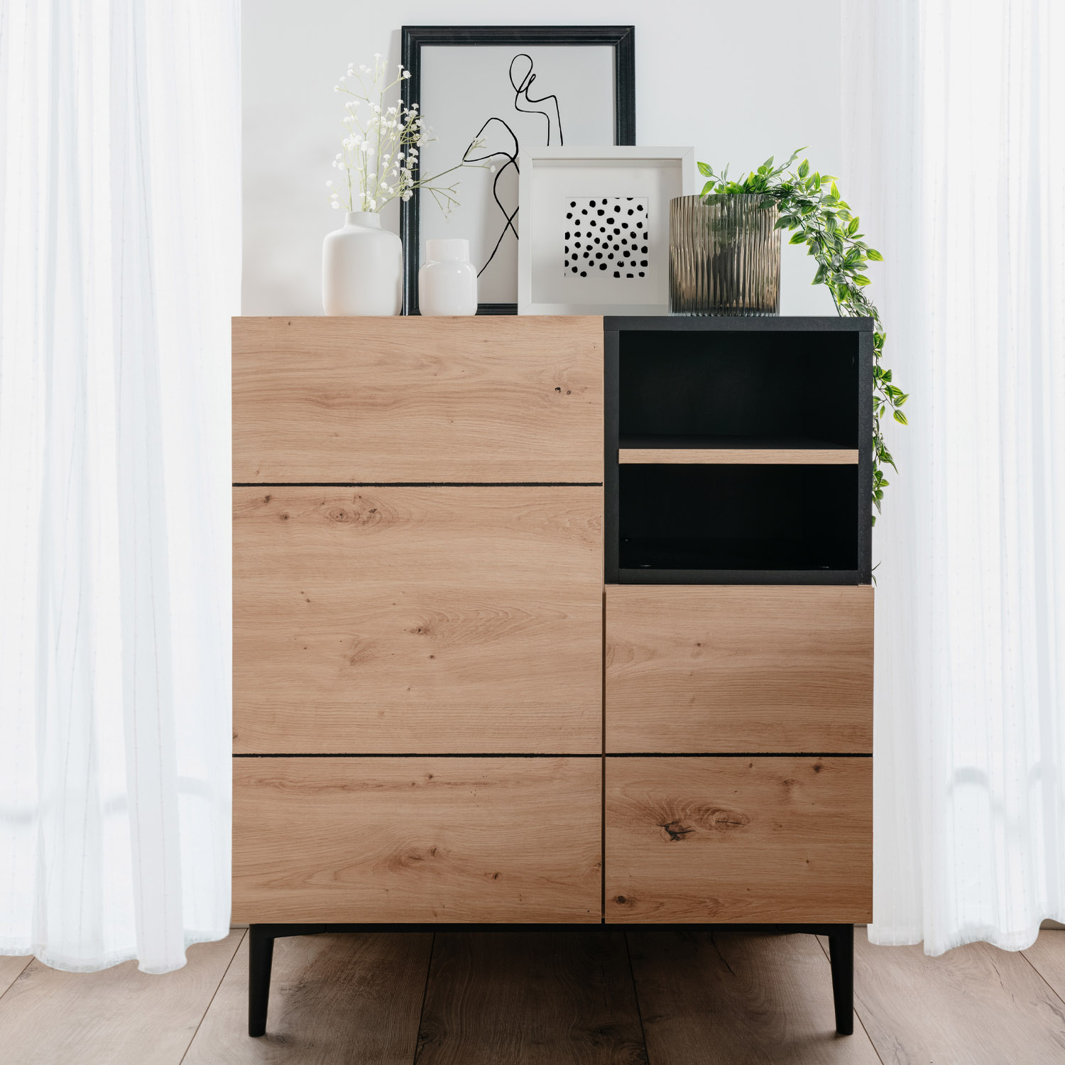 Kommode und Sideboard in Schwarz und Naturholzfarbe mit Oberflächen in Eichenoptik. Der Artikel ist freigestellt auf weißem Hintergrund abgebildet. Sichtbare Details sind Schubladenfronten, offene Ablagen, ein schwarzes Metallgestell und eine sichtbare Ho